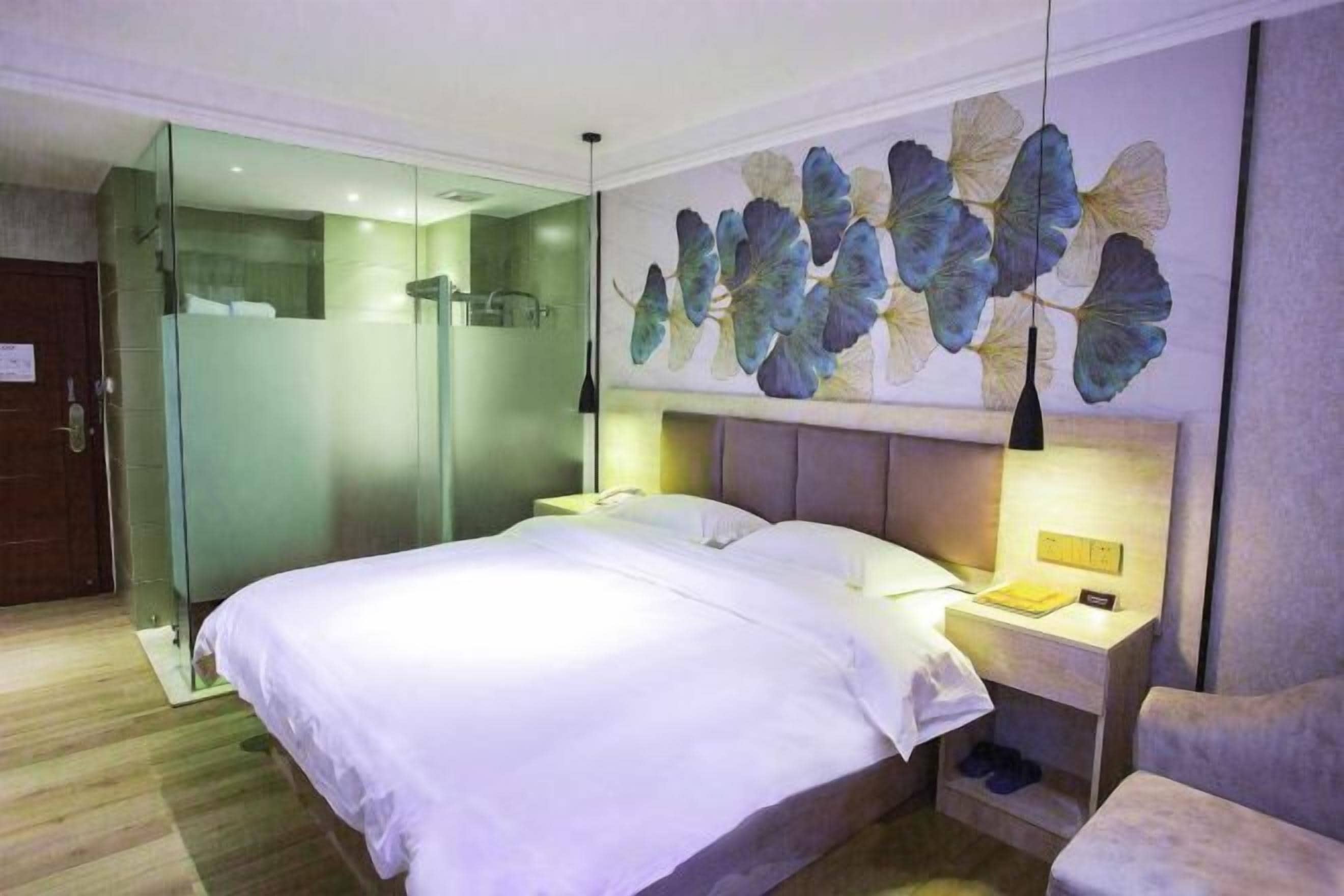 Quarto de hotel moderno com uma cama grande, chuveiro box em vidro e um mural decorativo na parede.