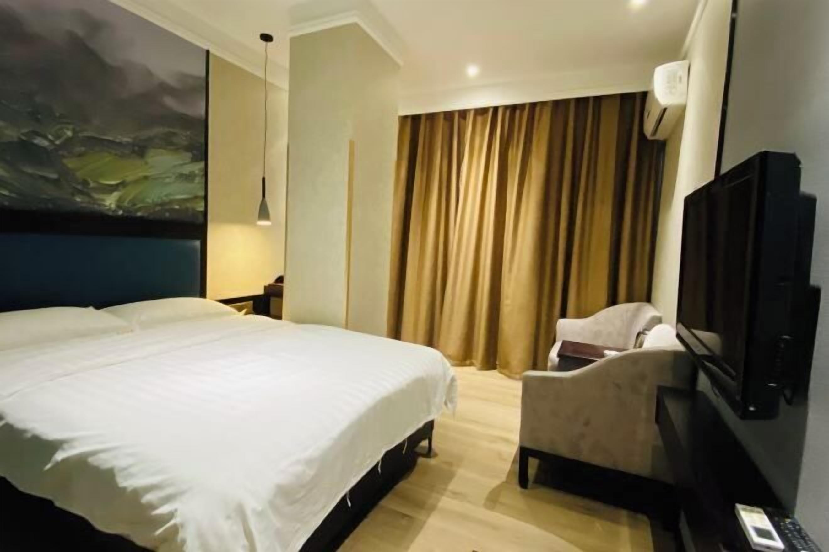 A hotel room with a bed, a chair, a television, and a painting on the wall.