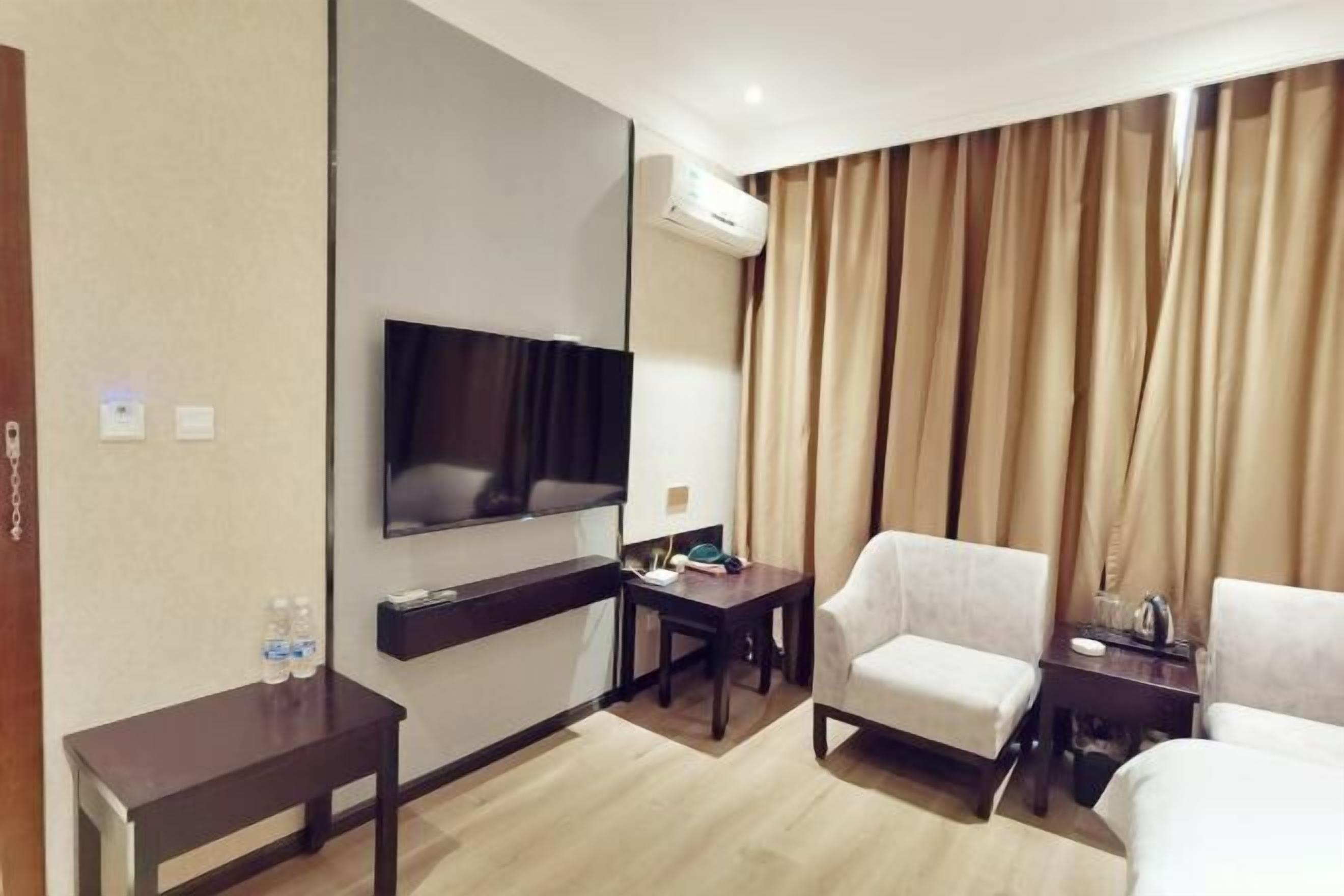 Habitación de hotel con televisión de pantalla plana, un escritorio, dos sillones, una mesita y una ventana con cortinas.