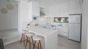 A modern kitchen with white cabinetry, a central island with stools, stainless steel appliances, and a view of the living area. - Protaras Holiday Villa Cr3 (Protaras)