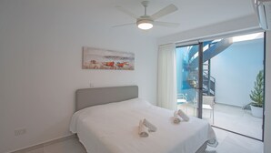 A bedroom with a bed, a ceiling fan, a painting, and a view of a balcony with a chair and a potted plant. - Protaras Holiday Villa Cr3 (Protaras)