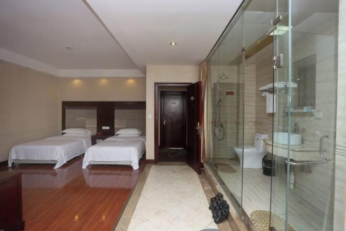 A hotel room with three beds, a glass shower enclosure, and a visible bathroom.