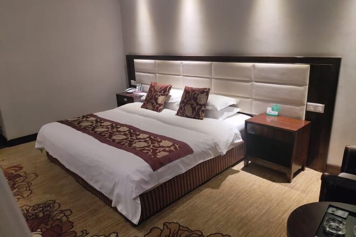 A hotel room with a large bed, a nightstand, a bedside table, and a chair.