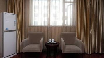 A hotel room with a wooden floor, two beige armchairs, a small round table with a tray, and a white refrigerator.