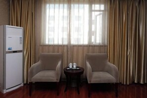 A hotel room with a wooden floor, two beige armchairs, a small round table with a tray, and a white refrigerator. - Huayuan Hotel (Zhongjiang)