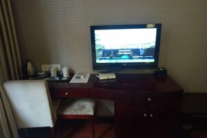 Habitación de hotel con escritorio, silla, televisor y un papel tapiz estampado.