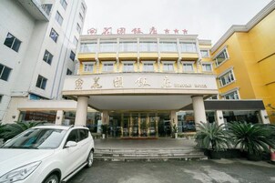 Entrada de hotel con fachada de vidrio y un coche blanco estacionado frente.