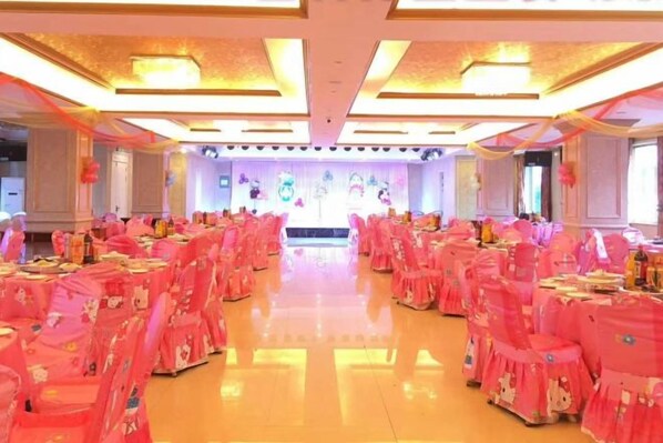 A banquet hall with rows of tables, chairs, and a stage.