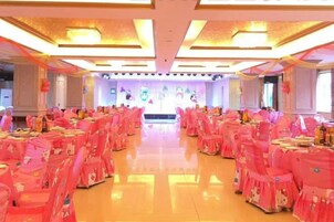 Un salón de banquetes con filas de mesas, sillas y un escenario.
