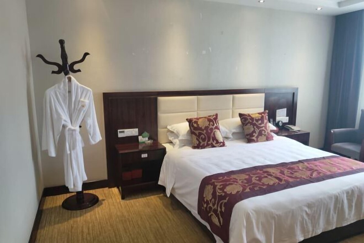 A hotel room with a large bed, a robe on a stand, a nightstand, and a chair.