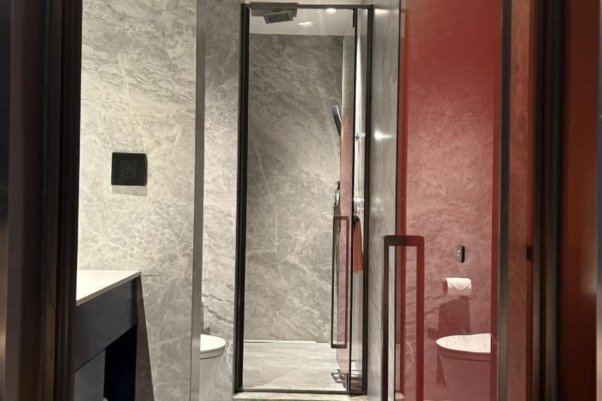 A modern bathroom with a glass-enclosed shower, marble walls, and a red accent wall.