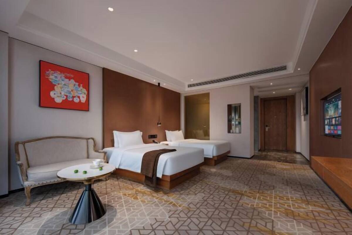 Ein Hotelzimmer mit zwei Betten, einem Sofa, einem kleinen runden Tisch und einem großen Fenster.