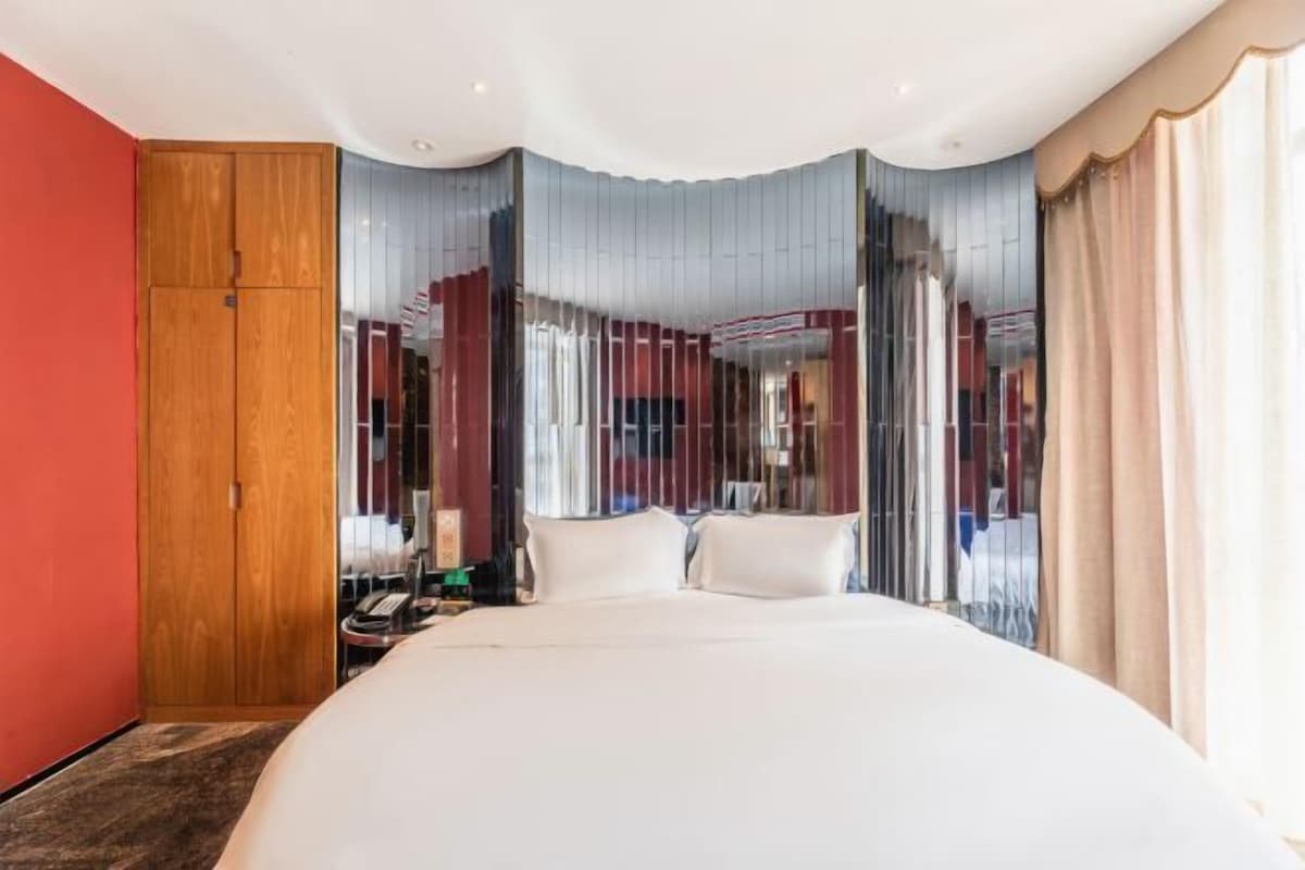 A modern hotel room with a large bed, a wooden wardrobe, and a view through sheer curtains.