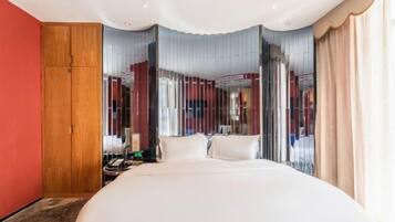 A modern hotel room with a large bed, a wooden wardrobe, and a view through sheer curtains.