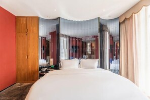 Een moderne hotelkamer met een groot bed, een houten garderobe en uitzicht door dunne gordijnen.