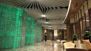 A modern hotel lobby with a green textured wall, a unique ceiling design, and a seating area with chairs and tables. - Greenman Lv Yijia Hotel (Poyang)