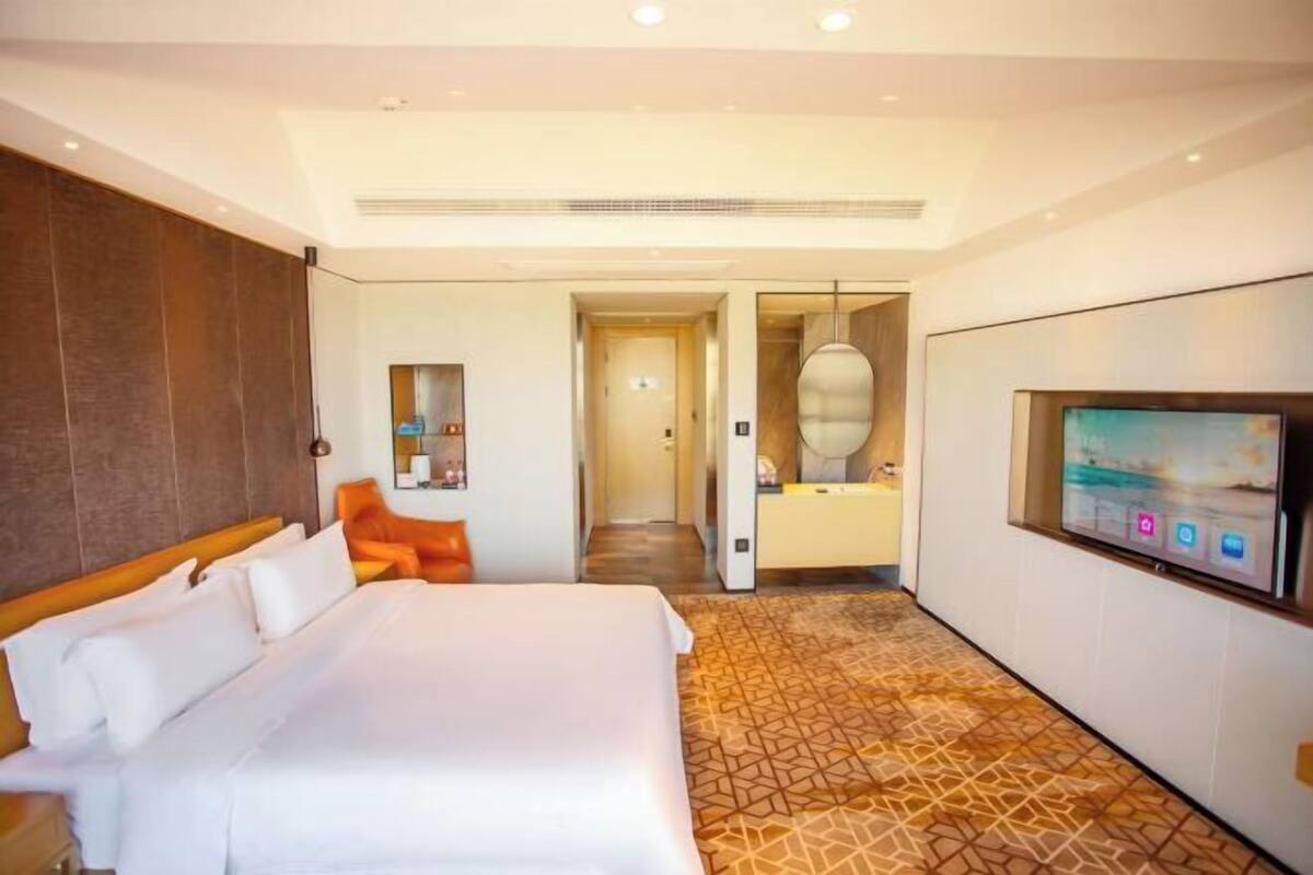 Ein Hotelzimmer mit einem großen Bett, einem Fernseher, einem Badezimmer und einem Gang zu einem weiteren Zimmer.