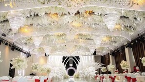 A banquet hall with a central stage, rows of white chairs with red sashes, and elaborate ceiling decorations. - Greenman Lv Yijia Hotel (Poyang)