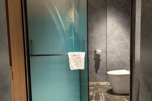 A bathroom with a glass shower enclosure, a toilet, and a towel hanging on the wall.