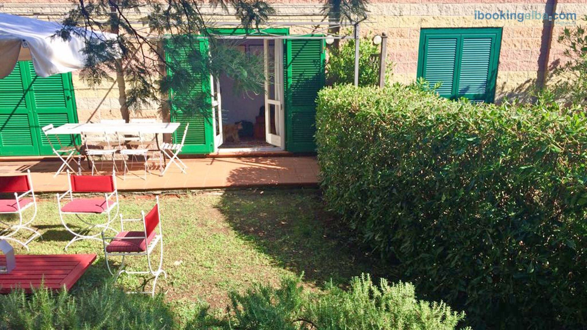 An outdoor patio area with a table and chairs, a covered seating area, and a hedge.