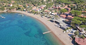 Une vue aérienne d’une ville côtière avec une plage, des eaux d’un bleu limpide et de nombreux bateaux.