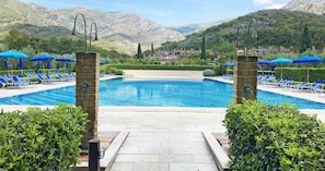 Une piscine entourée de verdure et de montagnes, avec des chaises longues et des parasols.