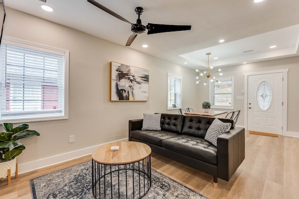A modern living room with a black leather sofa, a round coffee table, and a ceiling fan.