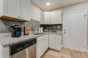 A modern kitchen with white cabinets, a granite countertop, a coffee maker, a dish soap dispenser, and a dishwasher.