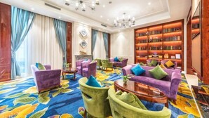 A hotel lobby with purple sofas, green armchairs, a patterned carpet, and a bookshelf. - Greentree Eastern Hotel (Jianhu Ouba Liya Life Square) (Jianhu)