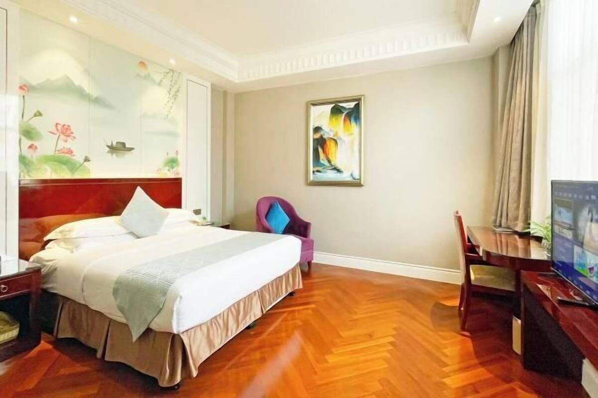 A hotel room with a bed, a chair, a television, and a wall with a painting.
