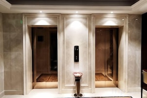 Un elevador moderno con pantalla digital, una pared de mármol pulido y una pequeña mesa con un florero.