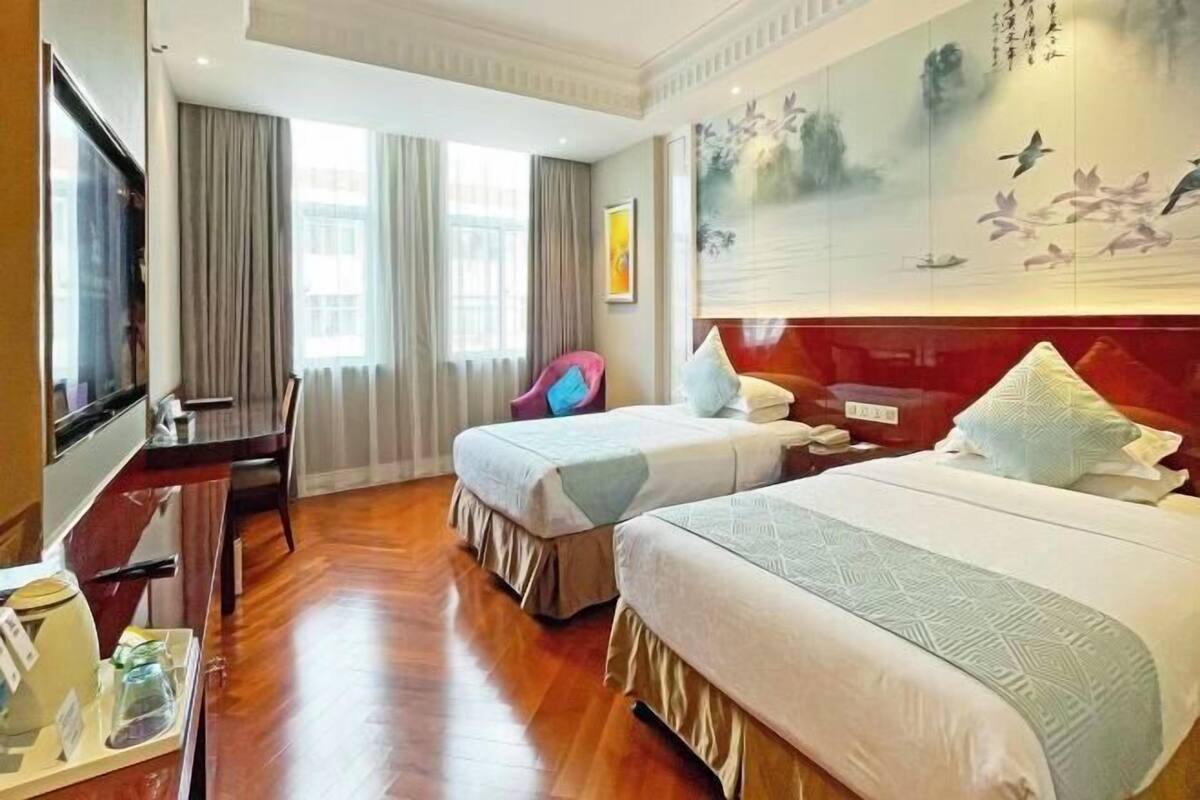 A hotel room with two beds, a desk, a chair, and a large painting on the wall.