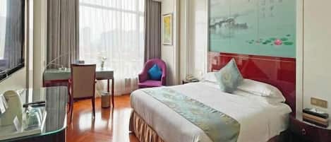 A hotel room with a large bed, a desk, a chair, and a window with curtains.