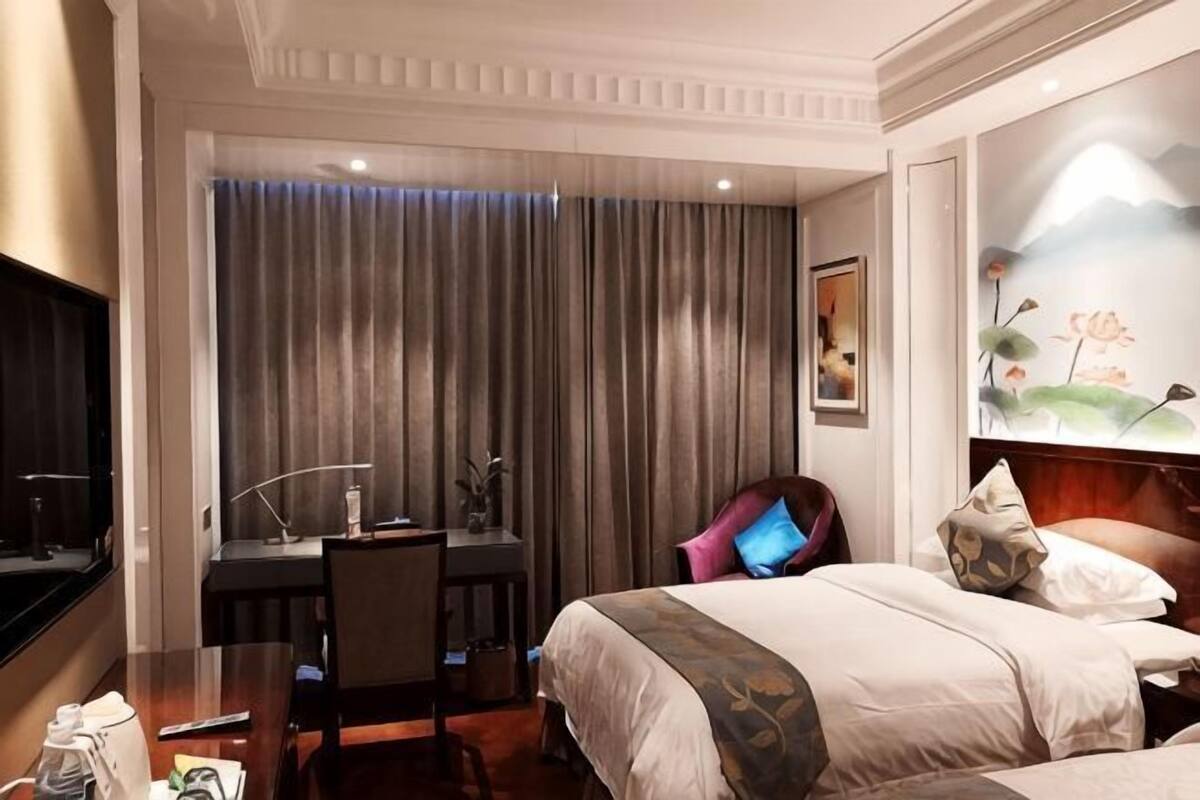A hotel room with a bed, desk, chair, and a painting on the wall.