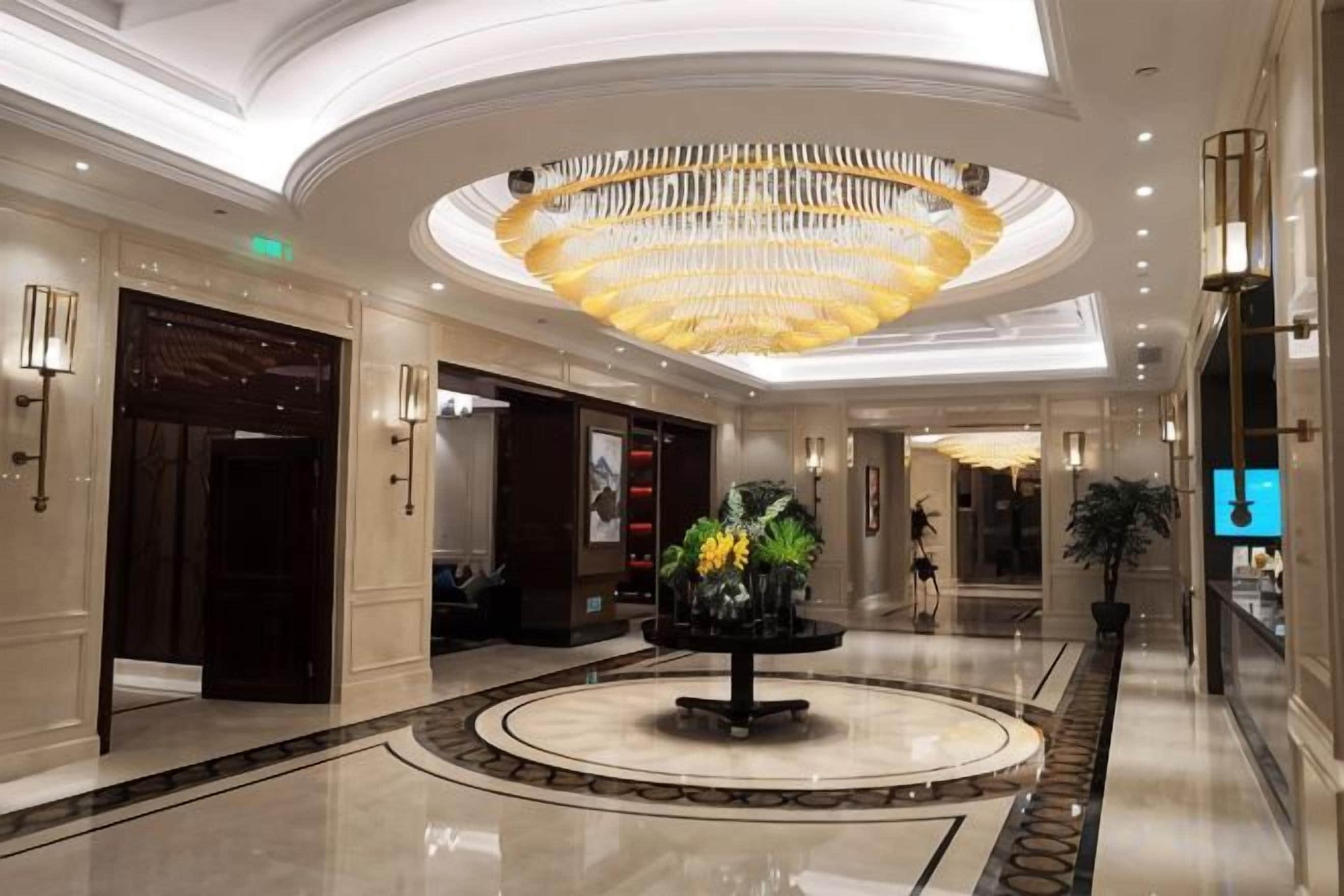 Un vestíbulo de hotel con una rotonda central, una gran araña y un mostrador de recepción.