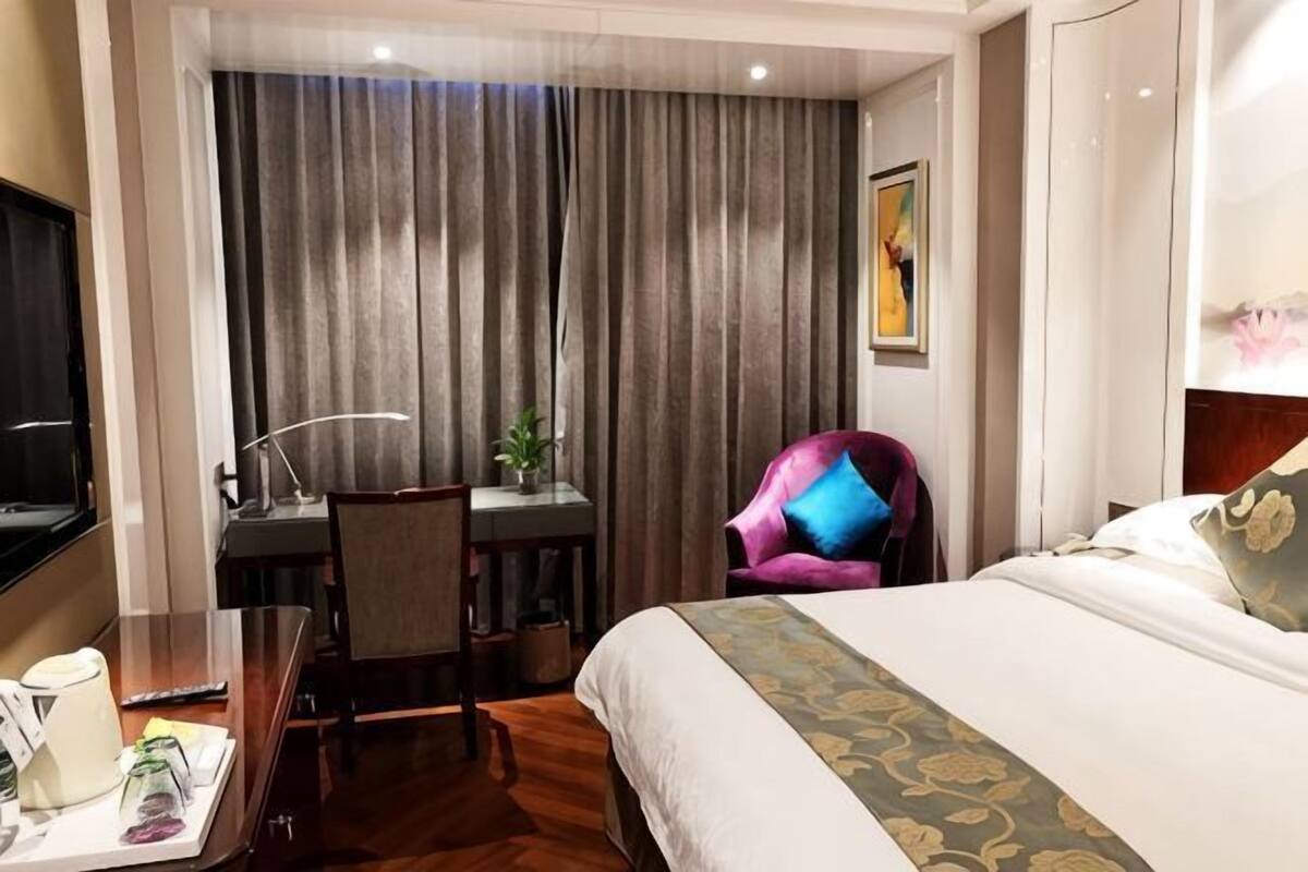 A hotel room with a bed, a desk with a chair, a television, and a window with curtains.