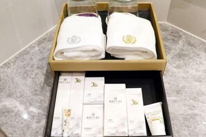 Una caja de madera con dos toallas blancas y varios artículos empaquetados sobre un piso de mármol.