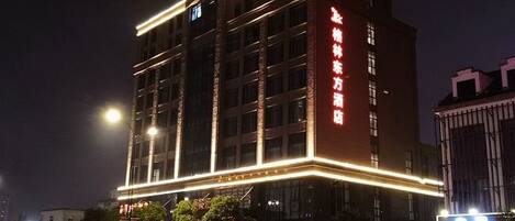 Un hotel de varios pisos con iluminación exterior, una entrada destacada y señalización en un idioma extranjero.