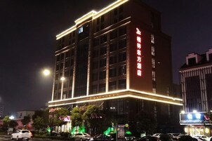 Um hotel com vários andares, iluminação externa vibrante, entrada imponente e sinalização em idioma estrangeiro.