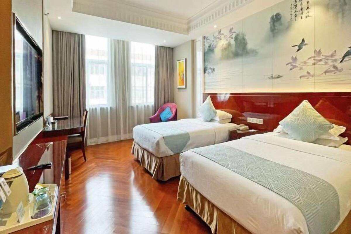A hotel room with two beds, a desk, a chair, and a large painting on the wall.