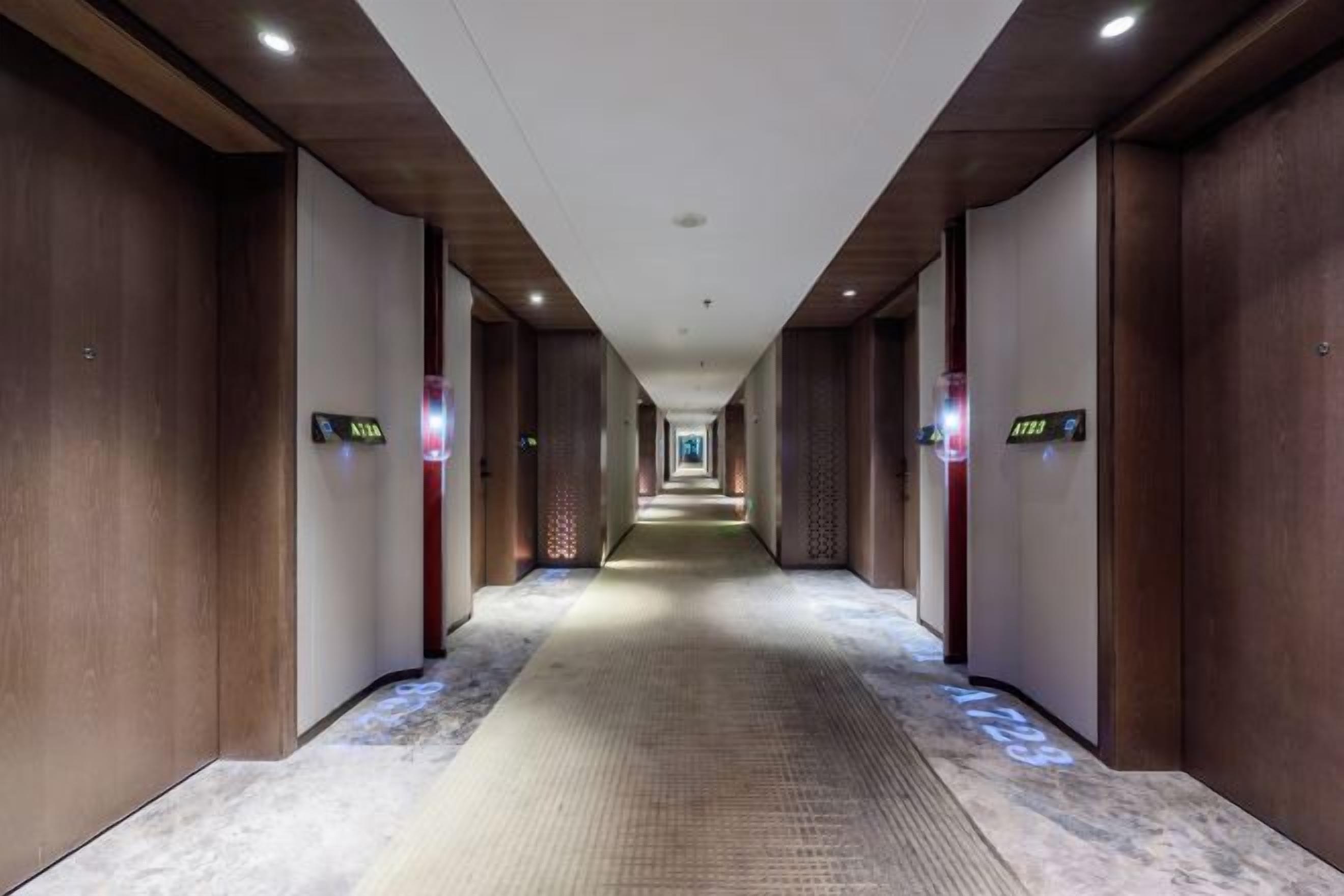 Un pasillo de hotel con paredes de madera, piso alfombrado y letreros iluminados que muestran los números de habitación.