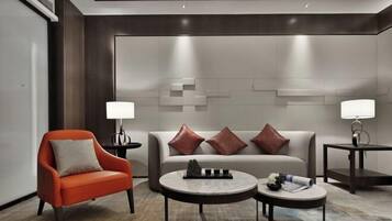 Una habitación de hotel moderna con sofá, sillón y dos mesitas de noche con lámparas.