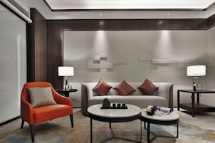 A modern hotel room with a sofa, armchair, and two side tables with lamps.