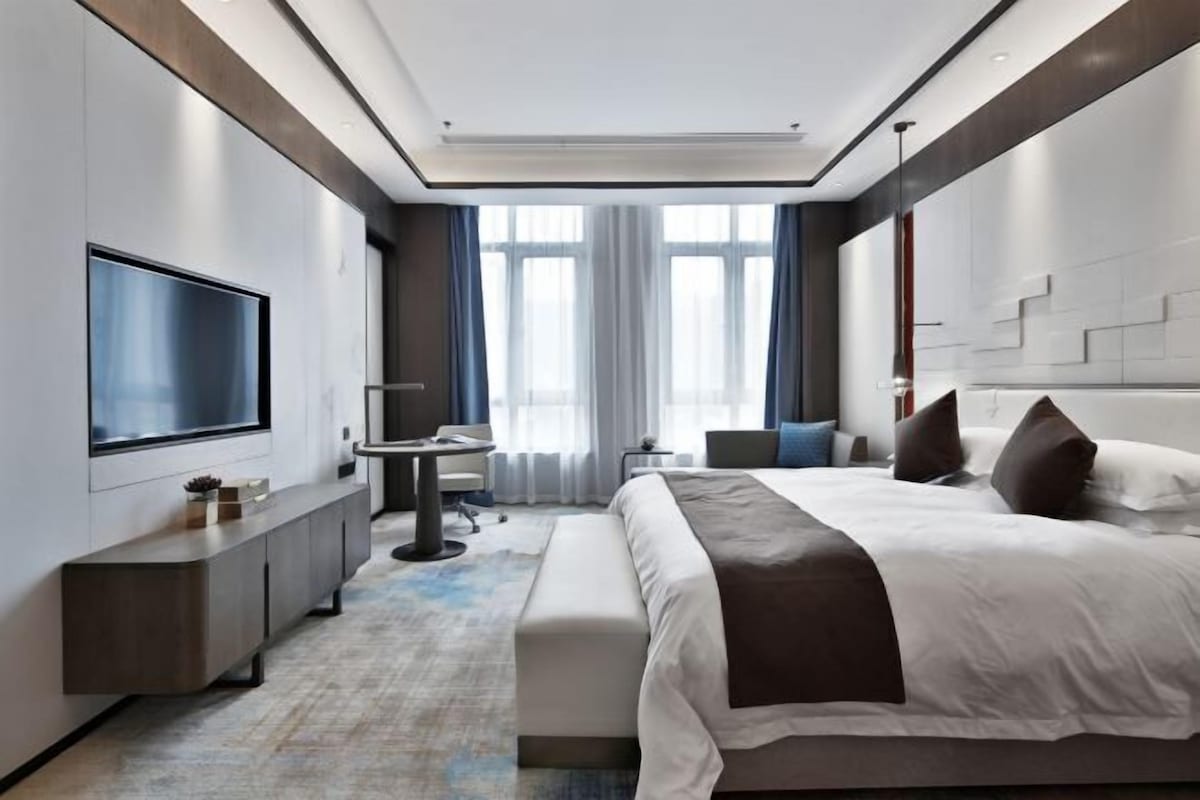 Una habitación de hotel moderna con una cama grande, un escritorio, un televisor de pantalla plana y una zona de estar.