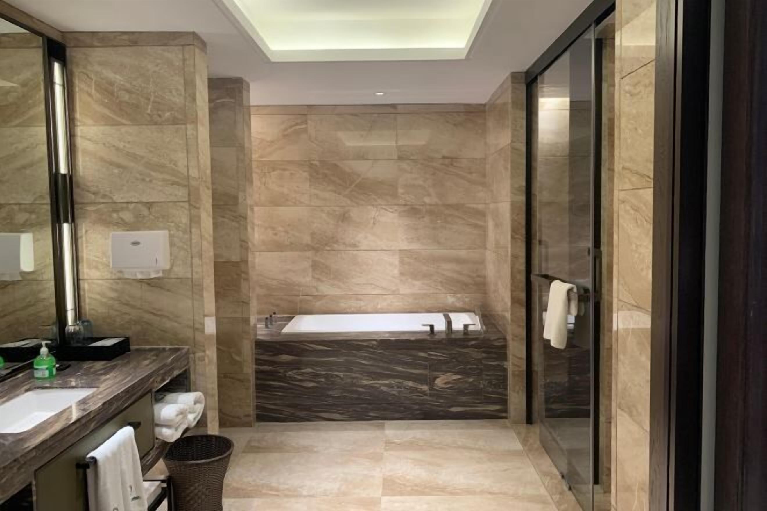 Une salle de bain moderne avec un meuble-lavabo en marbre, un grand miroir, une baignoire et une cabine de douche en verre.