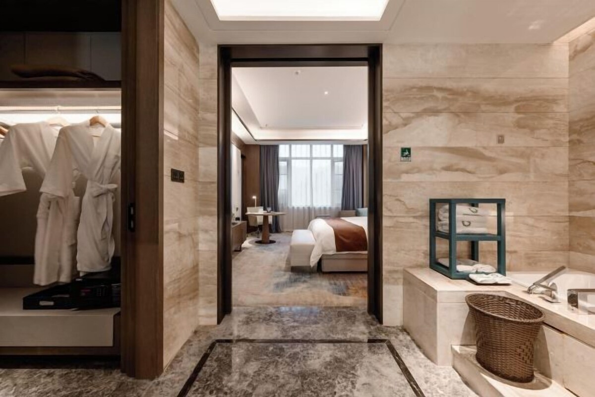 A hotel room with a bed, a bathroom, and a closet with hanging robes.