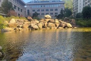 A calm river with large rocks in the foreground and a building with multiple windows in the background. - Feicui Zhouyu Hotel (Shicheng)