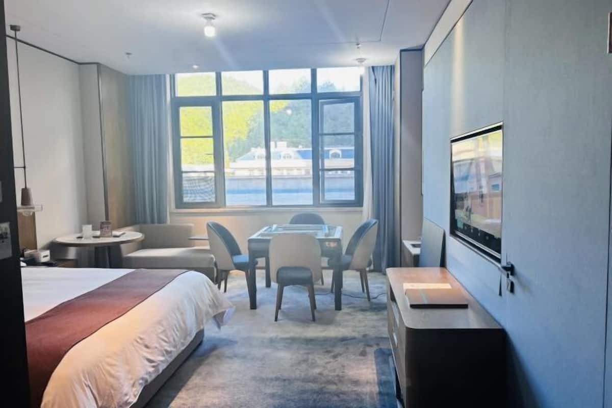 Hotellihuone, jossa on sänky, työpöytä, tuoli, pieni pöytä, televisio ja suuri ikkuna, josta avautuu näkymä vesistöön.