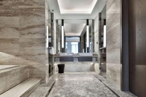 A modern bathroom with marble walls, a central sink, and a trash bin.