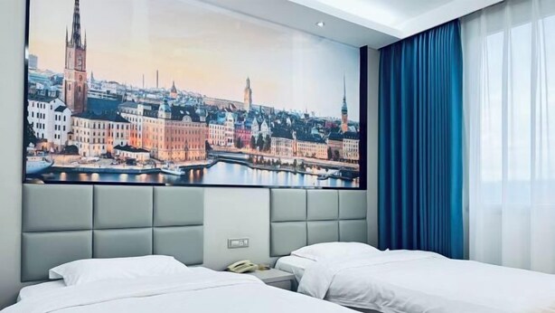 Quarto de hotel com duas camas, uma grande pintura de paisagem urbana na parede e um telefone na mesa de cabeceira.